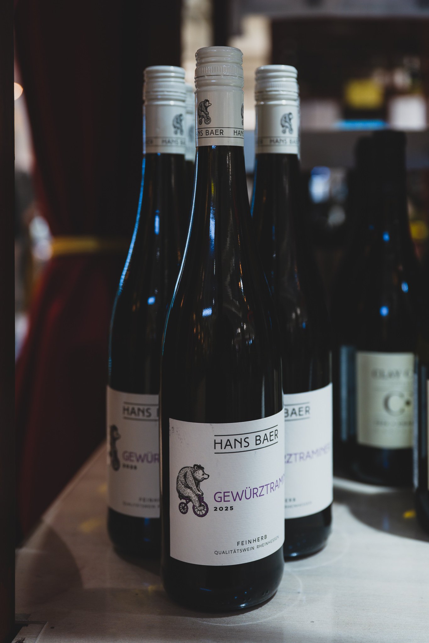 Three bottles of Hans Baer Gewürztraminer lined up on the counter, with a Clay Creek Chardonnay bottle blurred in the background