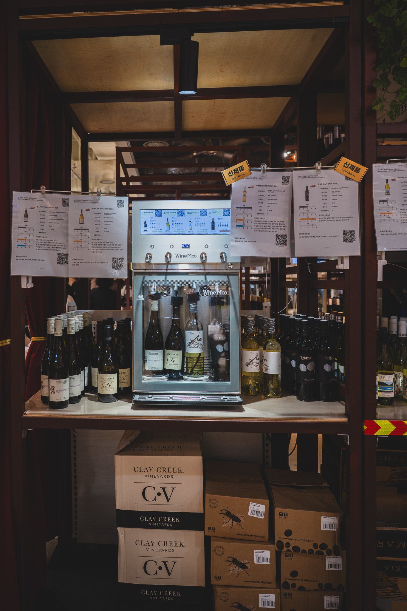 A WineMoo self-service tasting machine with four bottles loaded inside, surrounded by hanging tasting cards with QR codes and flavor charts
