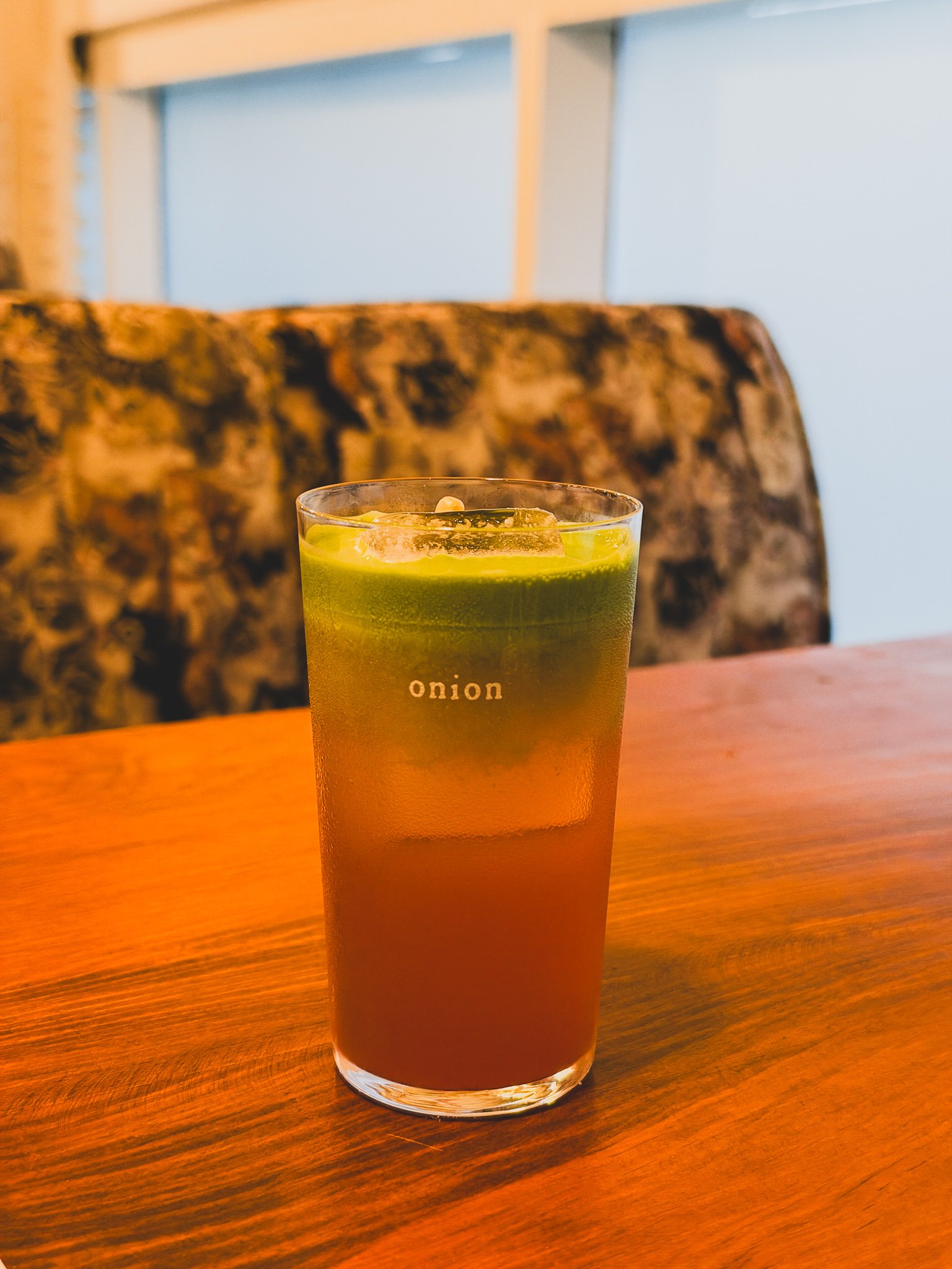 Close-up of the sujeonggwa drink topped with green matcha foam in a glass marked "onion"